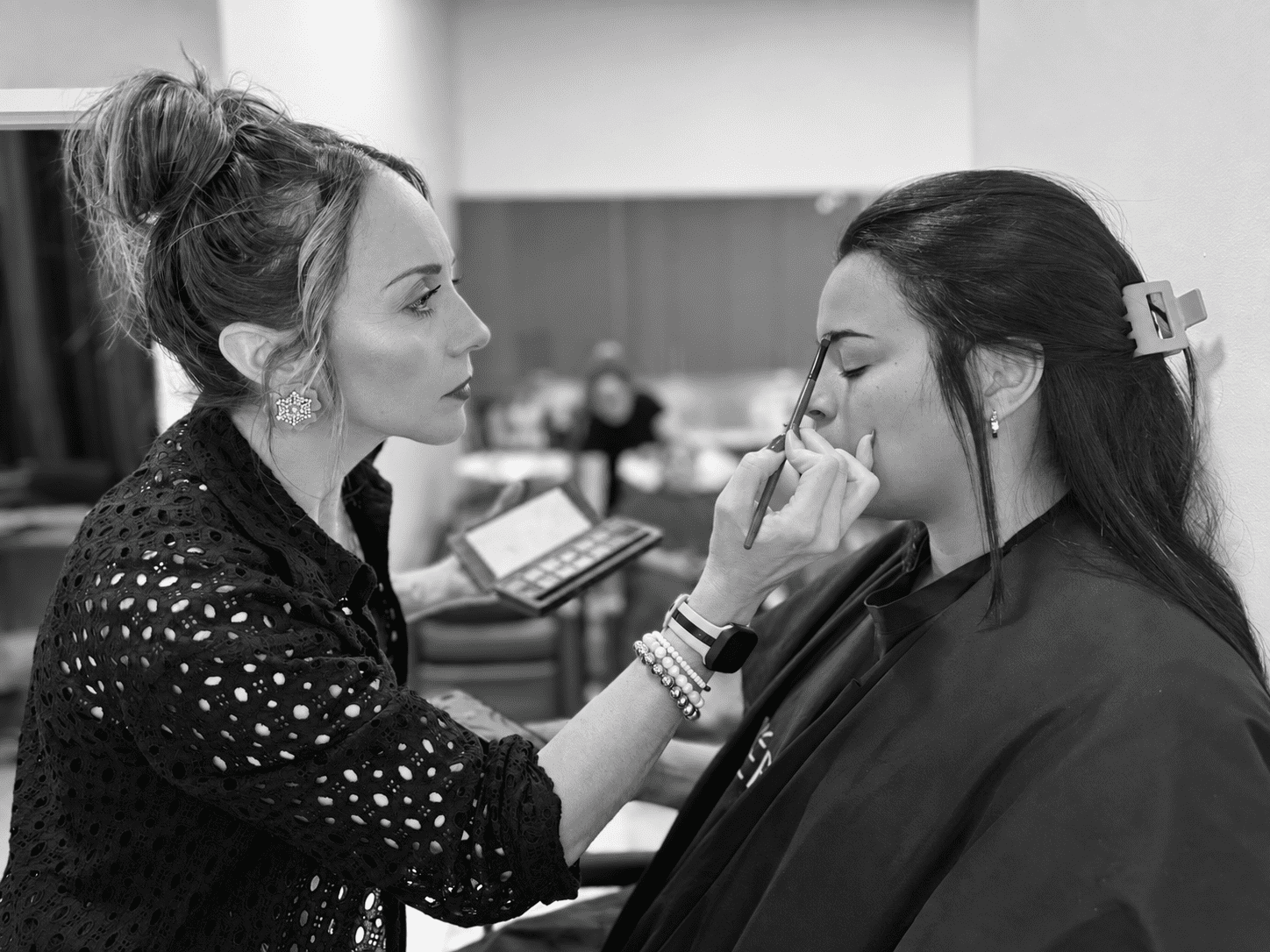 Makeup artist applying eyeshadow to a woman's eyelid in a salon setting.